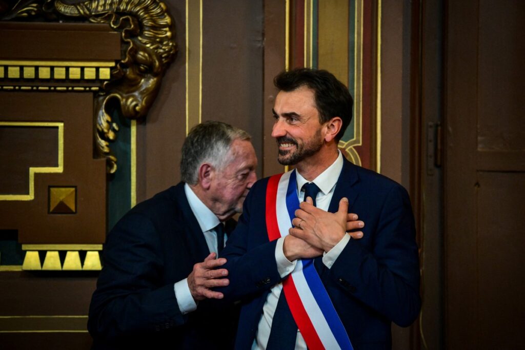 Gregory Doucet (à droite), récemment réélu maire de Lyon, réagit après avoir reçu son écharpe de maire des mains de Jean-Michel Aulas (à gauche), le 27 mars 2026.